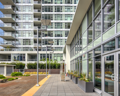 Modern urban terrace at the 510 Broadway complex in Seattle, featuring a landscaped communal area with wooden flooring, contemporary furniture, and a series of metallic poles, set against a backdrop of a multi-story residential building with large glass facades