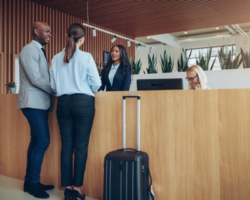 Guests checking in at the Denver Airport Premier Suites' front desk, with a man and a woman interacting with a hotel receptionist in a modern lobby, highlighting the hotel's welcoming and professional atmosphere