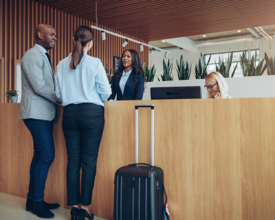 Guests checking in at the Denver Airport Premier Suites' front desk, with a man and a woman interacting with a hotel receptionist in a modern lobby, highlighting the hotel's welcoming and professional atmosphere