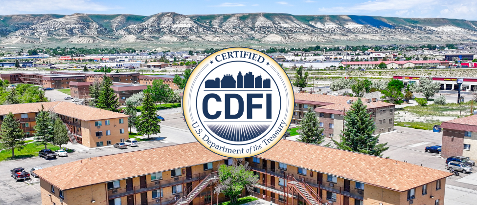 Aerial view of a low-income residential community with mountains in the background, highlighting the U.S. Department of the Treasury's Certified CDFI seal in the foreground, representing financial assistance for underserved areas.