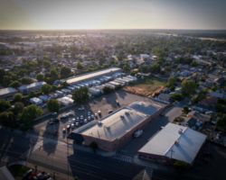 Aerial view of Victory Outreach Stockton's single-story building surrounded by a large parking lot, set against the backdrop of a residential neighborhood at sunrise.