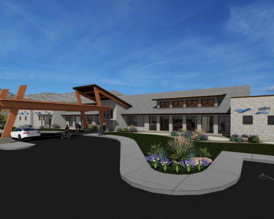 Architectural rendering of a modern healthcare facility featuring a spacious entrance with prominent wooden beams, stone walls, and landscaped areas, under a clear blue sky.